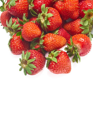 A group of ripe home grown strawberries, of different shapes and sizes, in bright red with green leaves gathered together at the top of the image on a white background, this creates an interesting pattern of colors and shapesの写真素材
