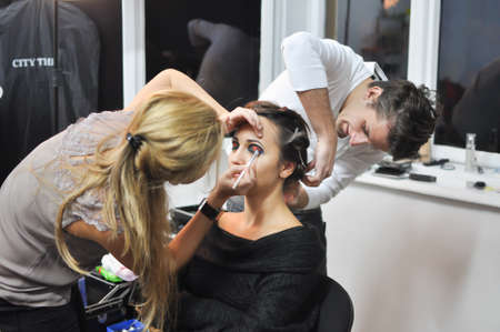 TIMISOARA, ROMANIA - November 10, 2012: Process of making makeup. Make-up artist working with brush on model face. Portrait of young brunette woman in beauty saloon interior. Applying tone to skin.のeditorial素材