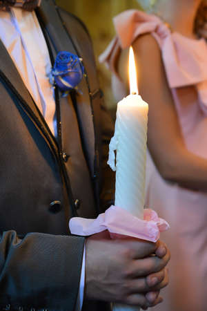 details of groom holding a white candle at the religious wedding ceremony