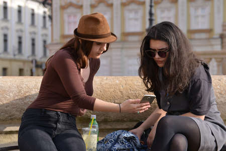 TIMISOARA, ROMANIA - April 18, 2018, Piata Unirii square: Happy female friends reading a text message outdoorsのeditorial素材