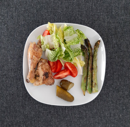 Homemade grilled chicken legs with grilled asparagus, green salad,  sliced tomatonand cucumber picklesy.の写真素材