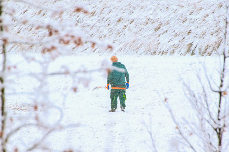 A worker carefully trims branches from a young tree on a cold snowy winter day outdoors.