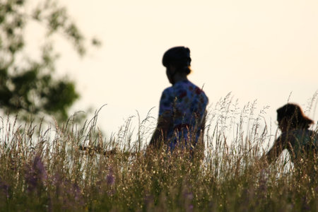 Silhouetted cyclists in floral and patterned clothes biking on rural path under golden lightの写真素材