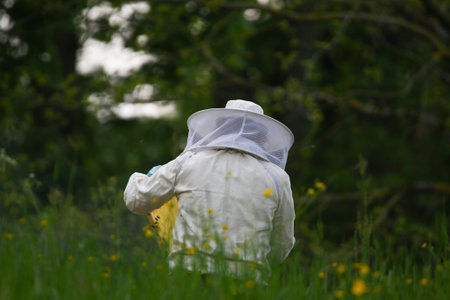 Beekeeper wearing full protective gear uses smoker while inspecting hive near vehicle spring meadowの写真素材