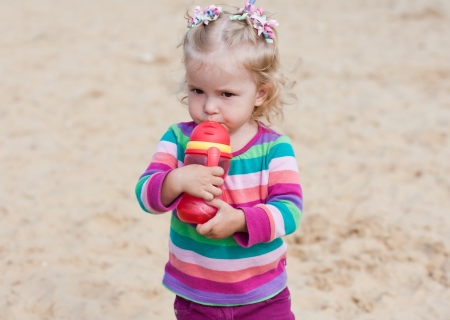 cute baby girl drinking from a bottle of red in natureの写真素材
