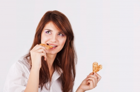 Portrait of young woman eating cookie heart-shaped on white backgroundの写真素材
