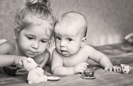 Cute little girl is playing with his younger brother at home lying on the bed with cupsの写真素材