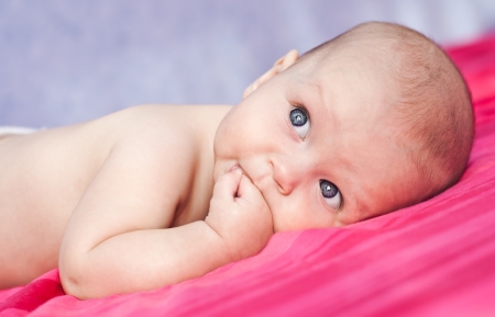 Cute happy baby thumb-sucking on a blue backgroundの写真素材