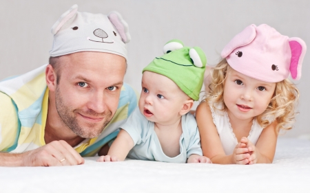 happy dad with kids in funny hats lying on the bedの写真素材