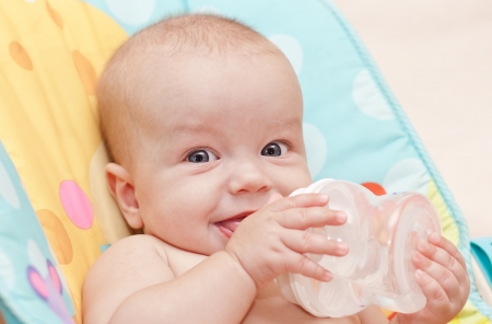 Happy baby holding a bottle and drink water looking at the cameraの写真素材