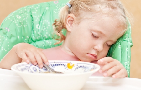 little girl fell asleep at the table eating soup with a spoon in his handの写真素材