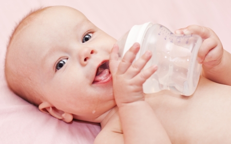 Happy baby holding a bottle and drink water looking at the cameraの写真素材