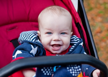 happy baby boy sitting in a red stroller and looking at the cameraの写真素材