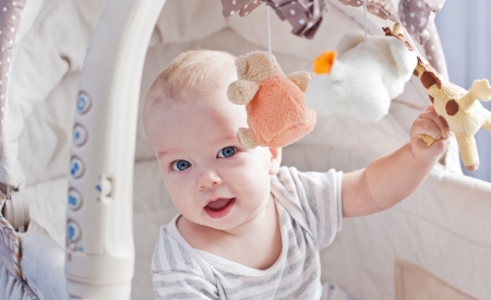 Baby boy playing sitting in the cradle with mobile toy giraffeの写真素材