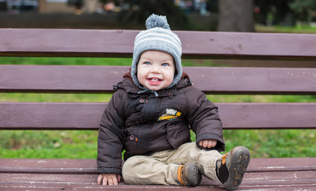 happy toddler boy sitting on the wooden bench