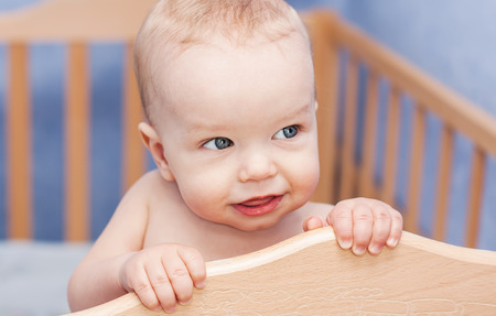 Cute toddler boy peeking out of the cot standingの写真素材