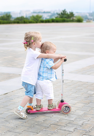 sister teaches toddler brother to ride a scooterの写真素材