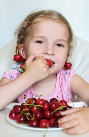 cute little girl eating cherries on white backgroundの写真素材