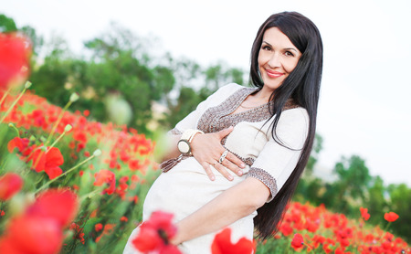 pretty pregnant brunette woman with poppy in field