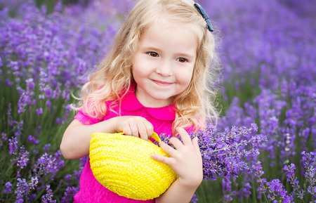 happy little girl is in a lavender field holds a basket of flowersの写真素材