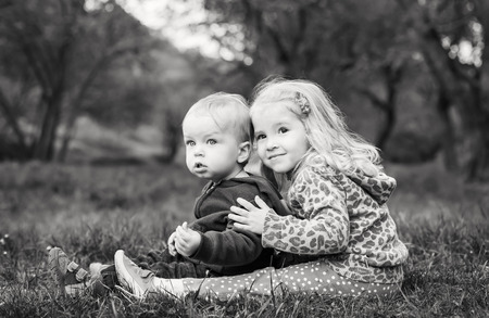  cute sister hugging brother sitting on the grass in the forest ( black and white )の写真素材