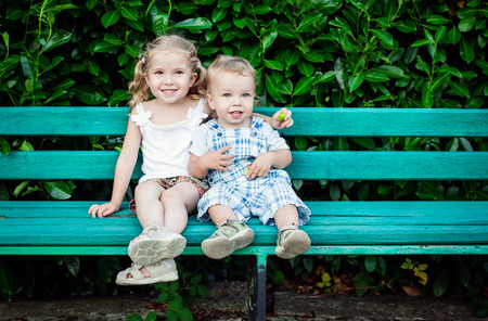 funny little children brother and sister sitting on benchの写真素材