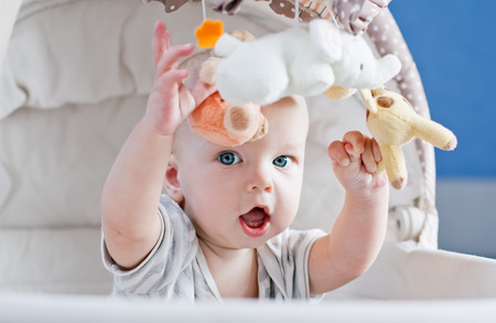 Baby boy playing sitting in the cradle with mobile toy 