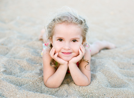 Happy little girl lying on the sand on the beachの写真素材
