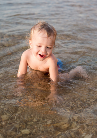Happy toddler boy playing on the sea at sunsetの写真素材
