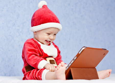 happy santa helper baby boy with digital tablet on a blue backgroundの写真素材