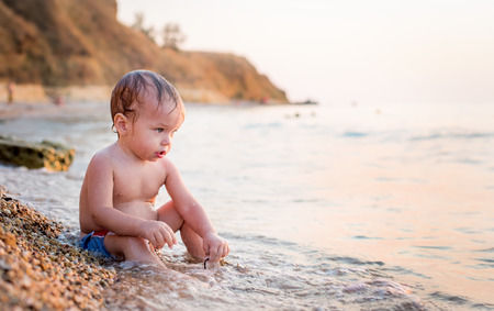 Happy toddler boy playing on the sea at sunsetの写真素材