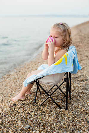 happy little girl on the beach sitting on a chair  drinking from a cup toyの写真素材