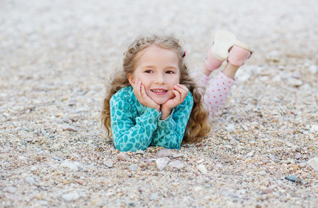 Happy little girl lying on the pebbles on the beachの写真素材