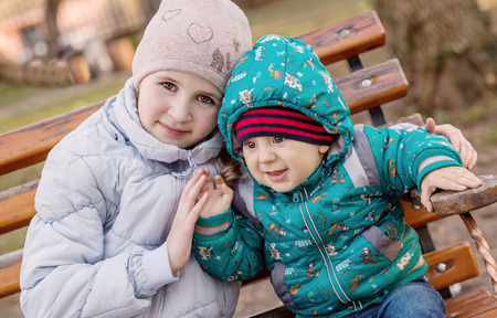funny little children brother and sister sitting on benchの写真素材