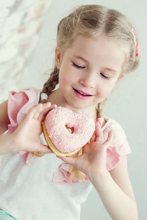 Happy little girl eating a donut in the shape of heartの写真素材