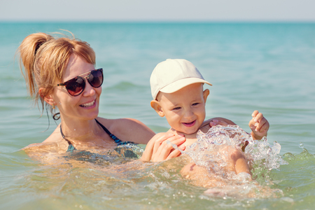 Happy mother playing with her little son at seaの写真素材