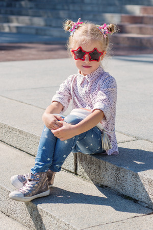 Adorable little girl sitting on stairs on warm and sunny summer dayの写真素材