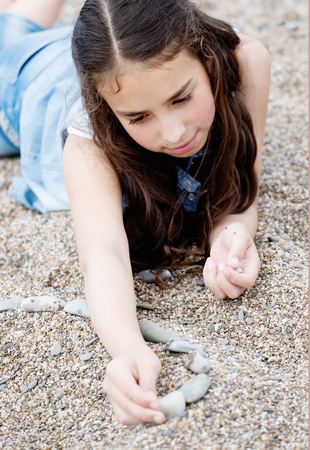 Girl playing with stones lying on the pebbles on the beachの写真素材