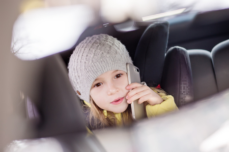 Mother driving car and child sitting on back seat and playing with mobile phoneの写真素材