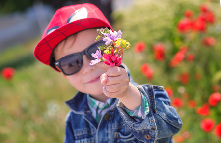 Funny little boy in sunglasses with a bouquet of wild flowersの写真素材