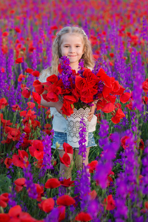 happy little girl in a field of poppies and purple wildflowersの写真素材