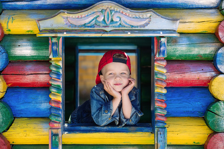 Cute little boy is playing on the playground, peeking out of the window of the houseの写真素材