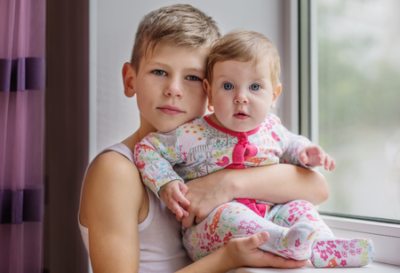 The elder brother hugs his baby sister at homeの写真素材