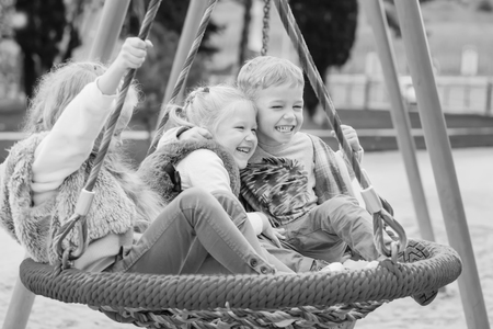 three children playing in the park with swing (black and white)の写真素材