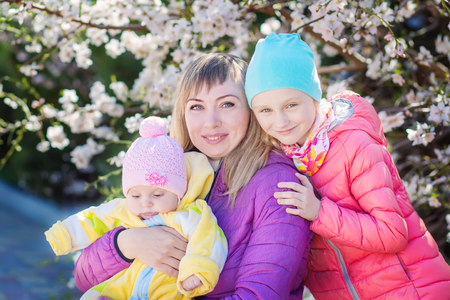 Happy mother with two little girls on the background of a flowering treeの写真素材