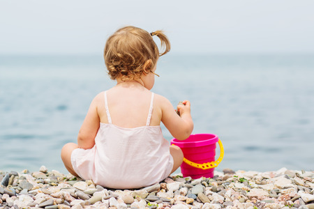 A little baby sits on a pebble beach and plays with pebblesの写真素材