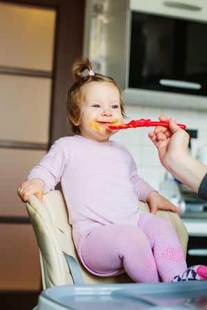 Feeding a happy baby with vegetable puree, standing on a chair for feedingの写真素材