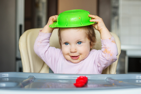 Happy little baby girl eats with a dirty face clothes on the head plateの写真素材