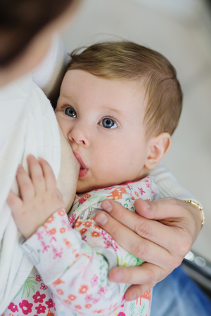 Close-up portrait of sweet newborn baby breastfeeding. Adorable new born caucaian kid holding moms finger with his cute little palm while breast feeding. Focus on hands. Young mother nursing babyの写真素材