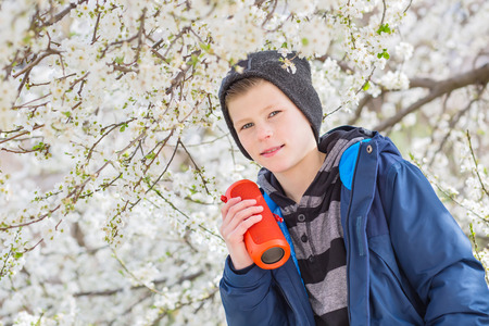 happy boy teenager with portable wireless speaker listening to music on the background of a blossoming treeの写真素材